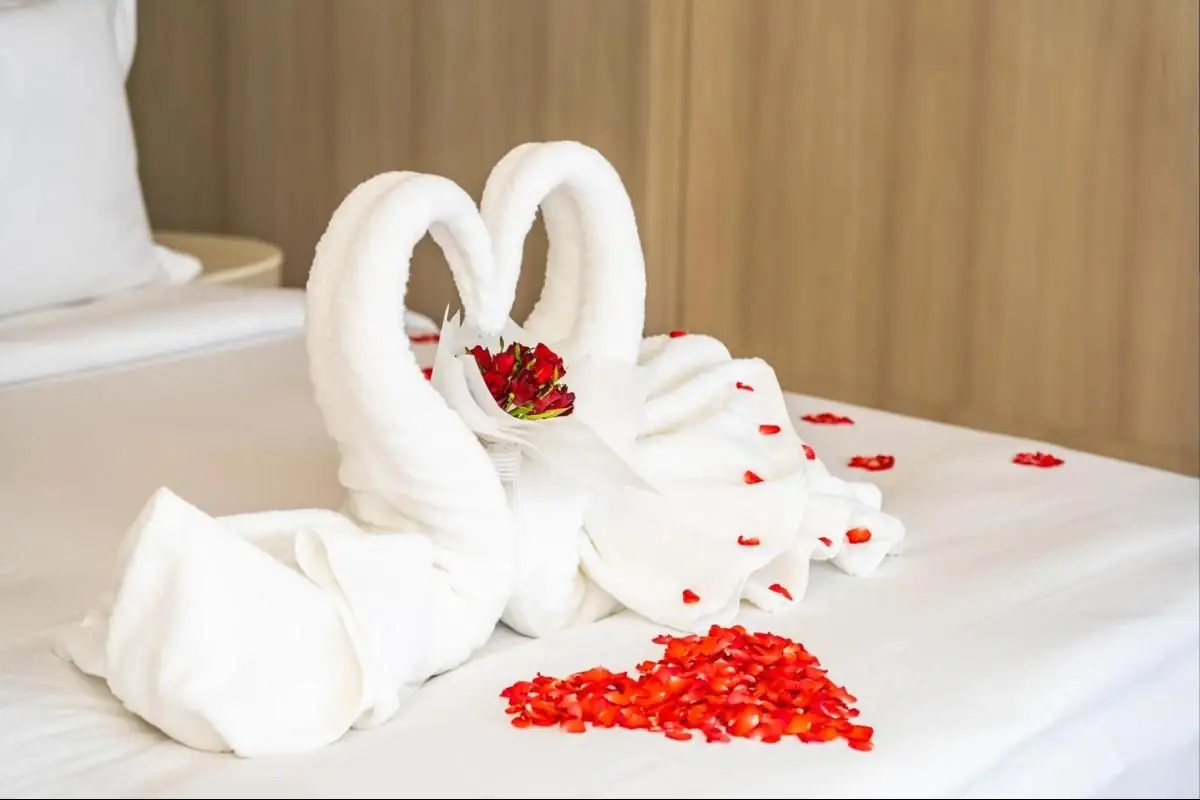 Toalhas em forma de cisnes formando um coração, com pétalas de rosas vermelhas